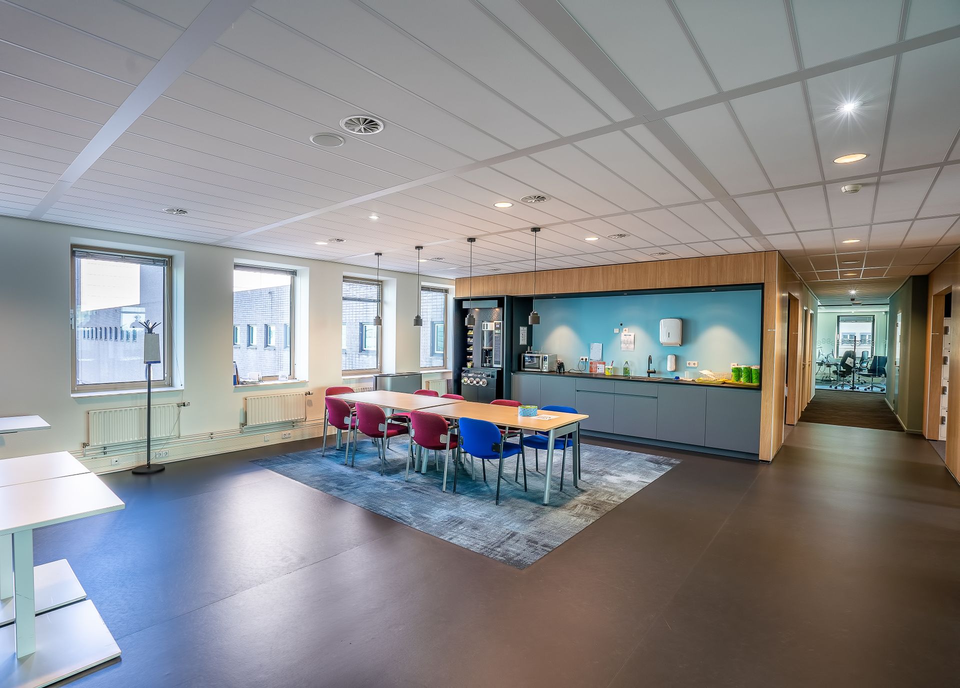 Spacious office kitchen and dining area with colorful chairs and sleek design.