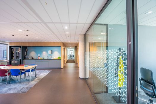 A sleek modern office space featuring colorful seating and a kitchenette in a bright, well-lit environment.