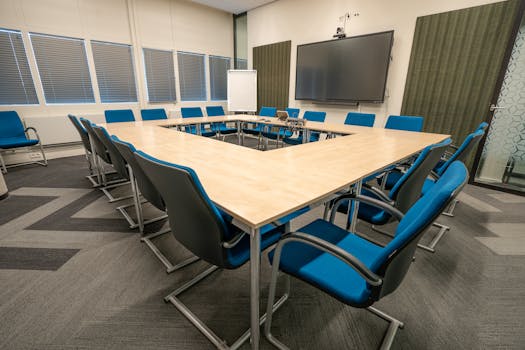 A modern conference room with a U-shaped table and blue chairs, perfect for meetings.