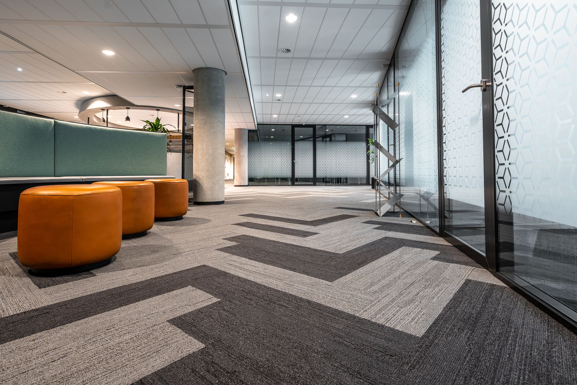 Spacious and modern office corridor featuring glass doors, geometric carpet patterns, and leather seating