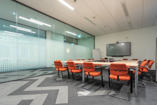 Spacious conference room with glass walls and orange chairs around a rectangular table.