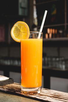 Tall glass of orange juice with a lemon slice and straw, perfect for a refreshing drink.