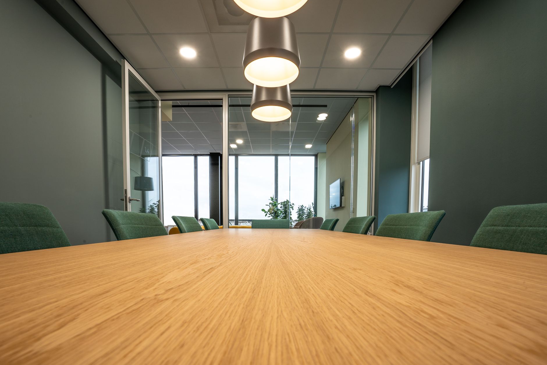 Spacious conference room with sleek wooden table, green chairs, and pendant lighting highlighting a minimalist style.