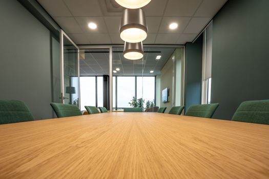 Spacious conference room with sleek wooden table, green chairs, and pendant lighting highlighting a minimalist style.