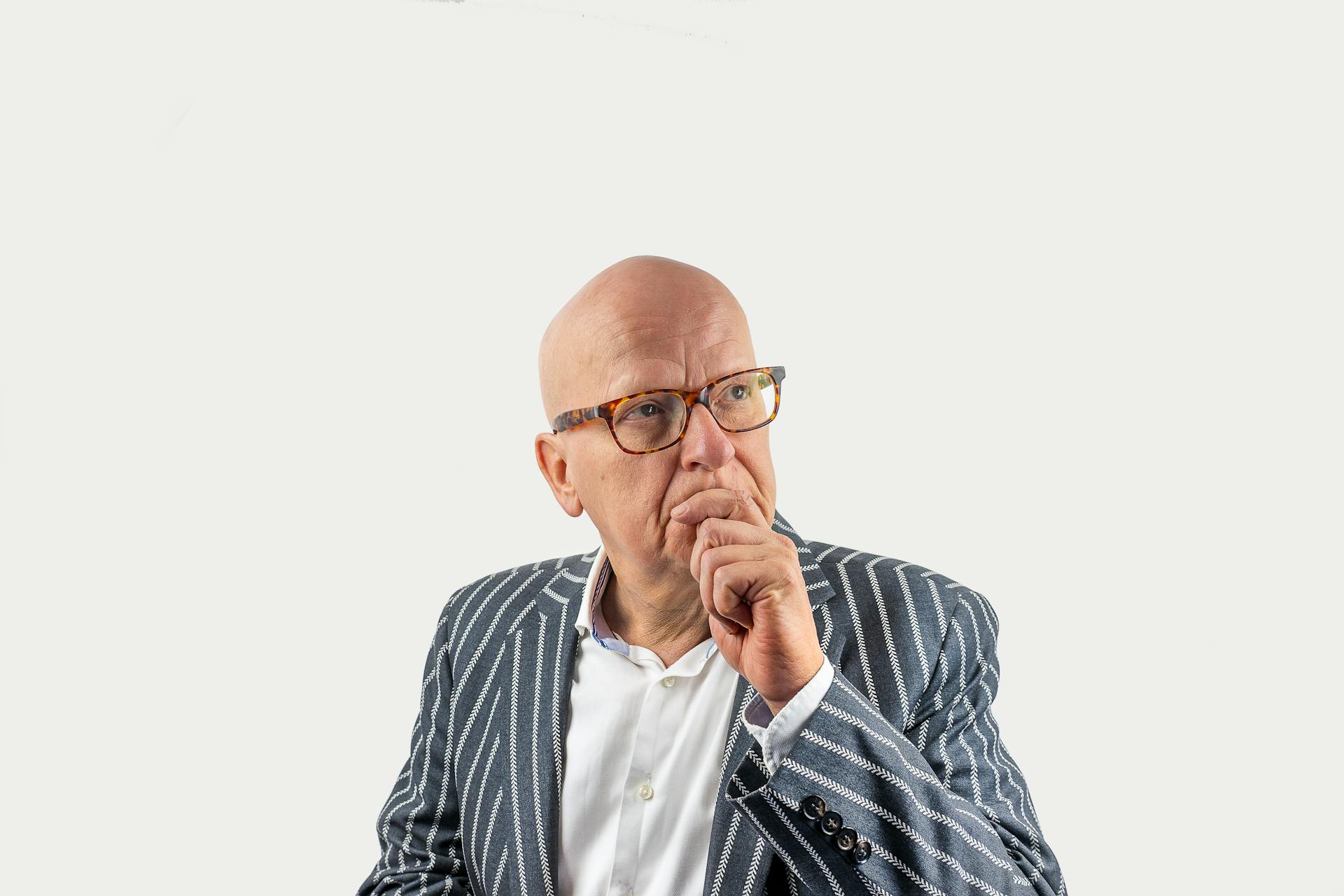 Portrait of an elderly businessman in a striped suit and eyeglasses, deep in thought, on a white background.