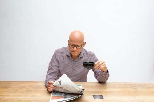 Free Elderly man enjoying a newspaper and coffee indoors on a wooden table. Stock Photo