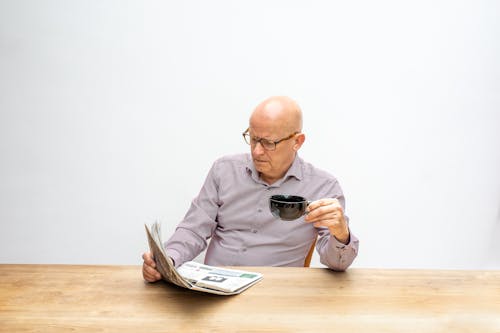 Free Man in Long Sleeve Shirt Holding a Cup of Coffee and Newspaper Stock Photo