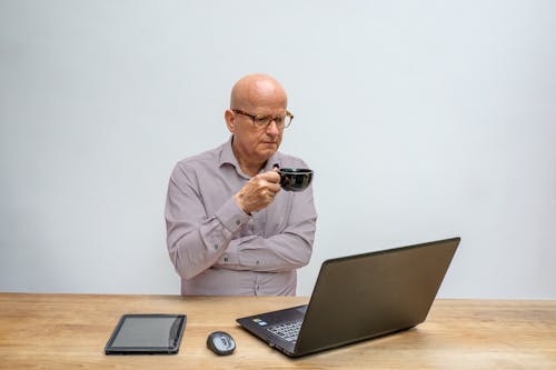 A Man Having Coffee While Looking at a Laptop