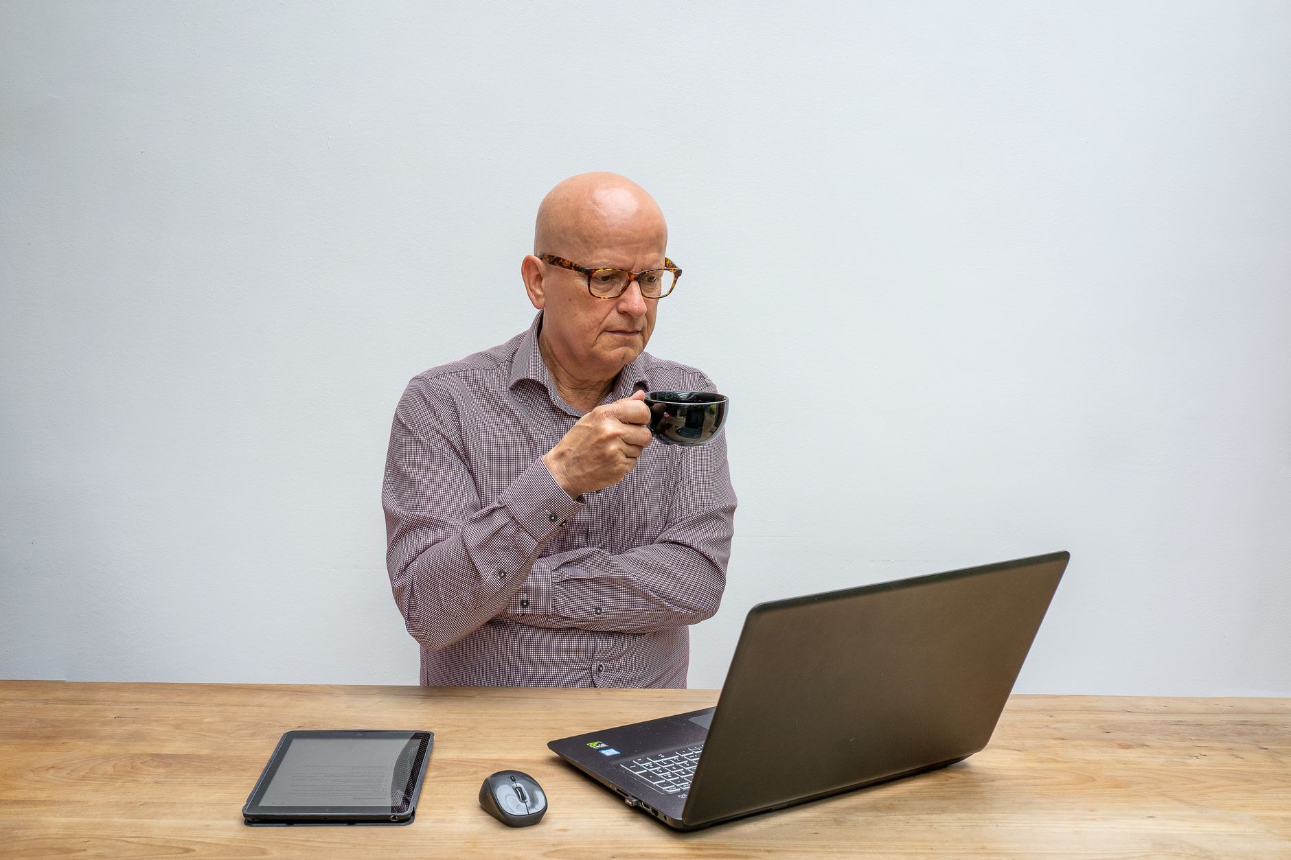 A thoughtful elderly man using a laptop while sipping coffee, epitomizing remote work.