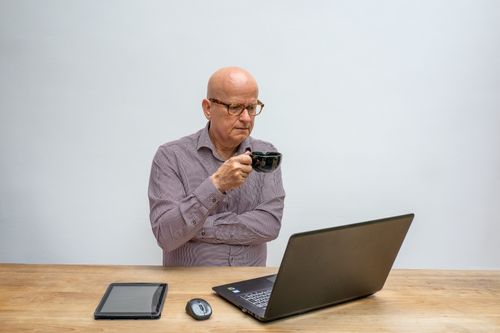 Free A thoughtful elderly man using a laptop while sipping coffee, epitomizing remote work. Stock Photo