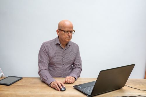 Free Elderly man using laptop and mouse, focused at work in a bright setting. Stock Photo
