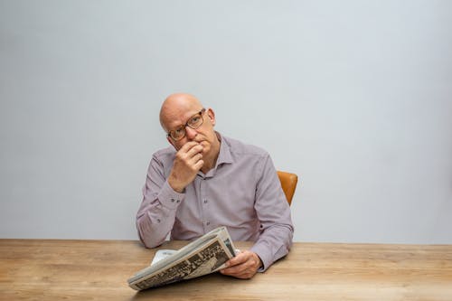 Free A Man Contemplating While Holding the Newspaper Stock Photo