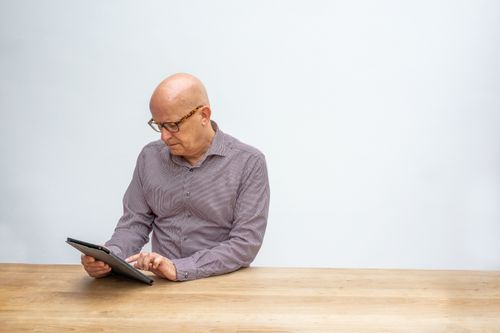 Free Elderly man in glasses using a tablet on a wooden table against a white background. Stock Photo