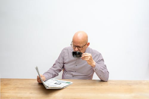 A Man Drinking a Cup of Coffee While Reading a Newspaper