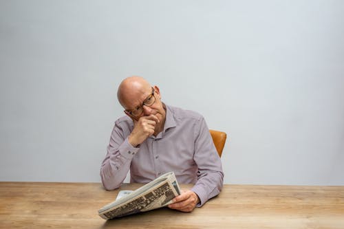 Man in Gray Long Sleeve Shirt and Eyeglasses Holding a Newspaper