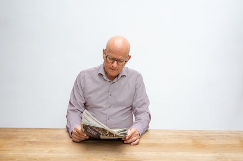 A Man Wearing Gray Polo Shirt is Reading a Newspaper