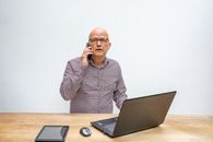 Man in Gray Zip Up Jacket Sitting Beside Brown Wooden Table With Macbook Pro