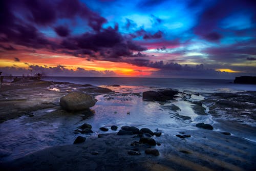 Free Sunset under Clouds over Rocks on Sea Shore Stock Photo