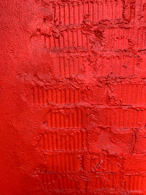 Close-up of a vibrant red textured wall showcasing rough concrete and paint details.