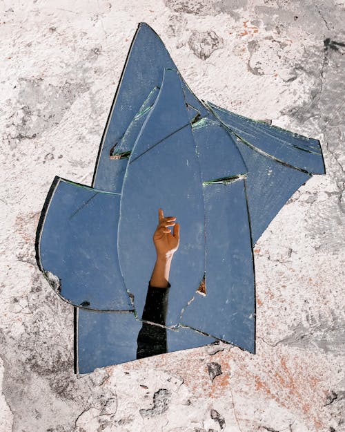 Mirror Fragments on Gray Surface With The Reflection Of A Person's Hand