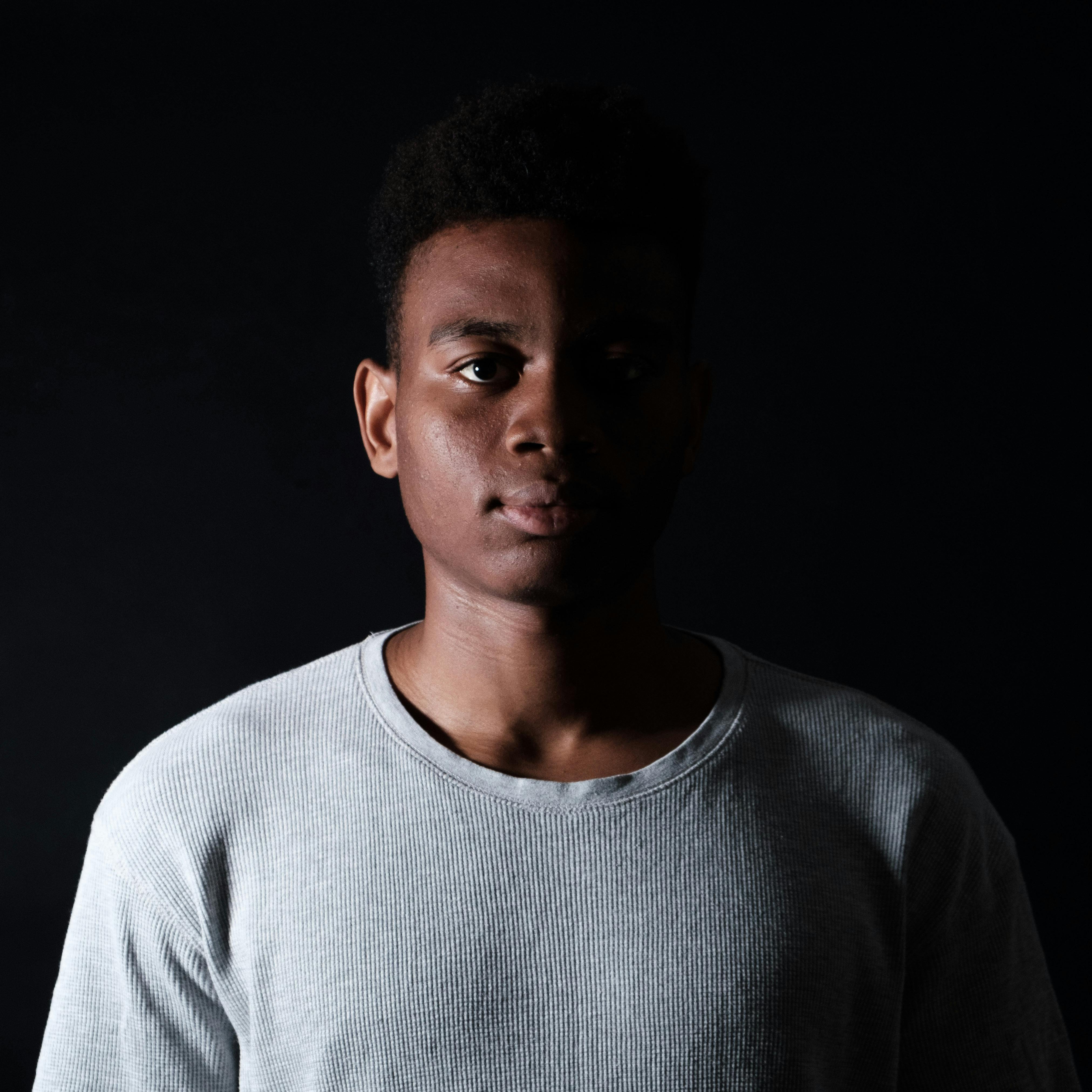 Portrait of young African American male in casual outfit looking at camera on black background