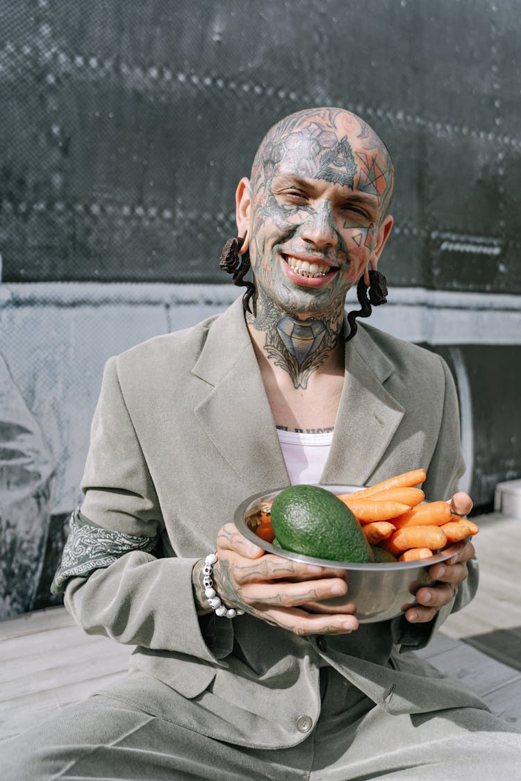 Tattooed Man Holding A Bowl Of Fresh Fruit And Vegetable