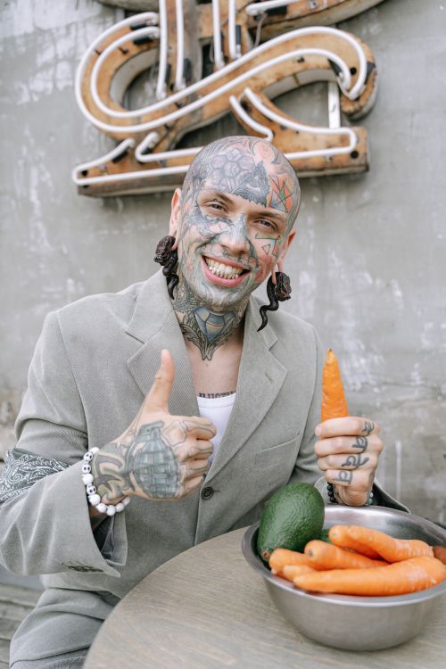 Free A tattooed man in formal attire holding a carrot and smiling confidently. Stock Photo
