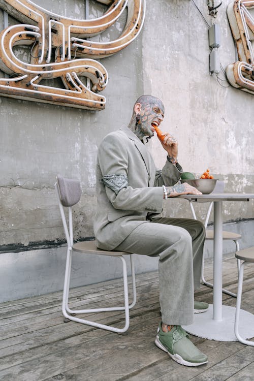 Tattooed Man in Gray Blazer eating Carrots 