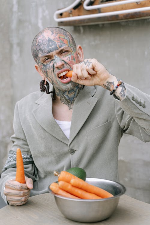 Tattooed Man in Gray Blazer eating Carrots