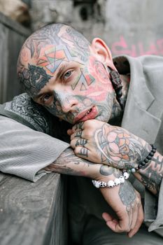 一名纹身男子在户外沉思的特写肖像，清晰展示了他面部和手部的复杂纹身