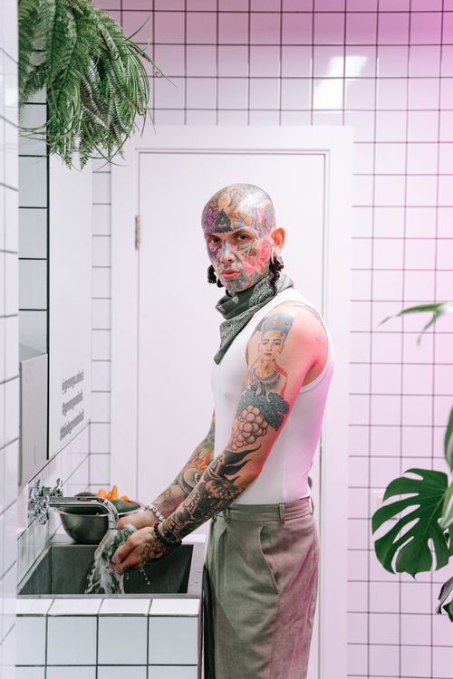 Free Colorful tattoos adorn a man washing hands in a sleek tiled bathroom. Stock Photo