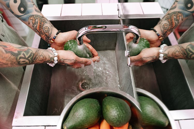 Tattooed Person Washing Avocados On A Sink 