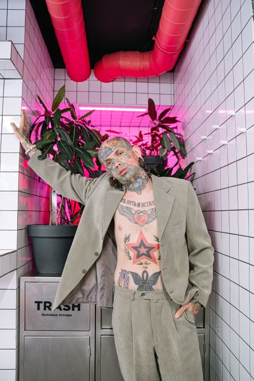 Free A tattooed man poses stylishly in a suit against a modern, vibrant background. Stock Photo
