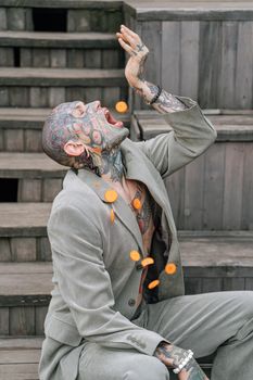 一名纹身男子穿着西装，坐在户外的楼梯上，高兴地把切好的胡萝卜扔向空中