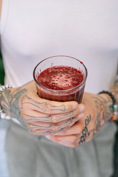 Free Close-up of tattooed hands holding a glass of fresh berry juice, capturing intricate ink designs and vibrant drink. Stock Photo