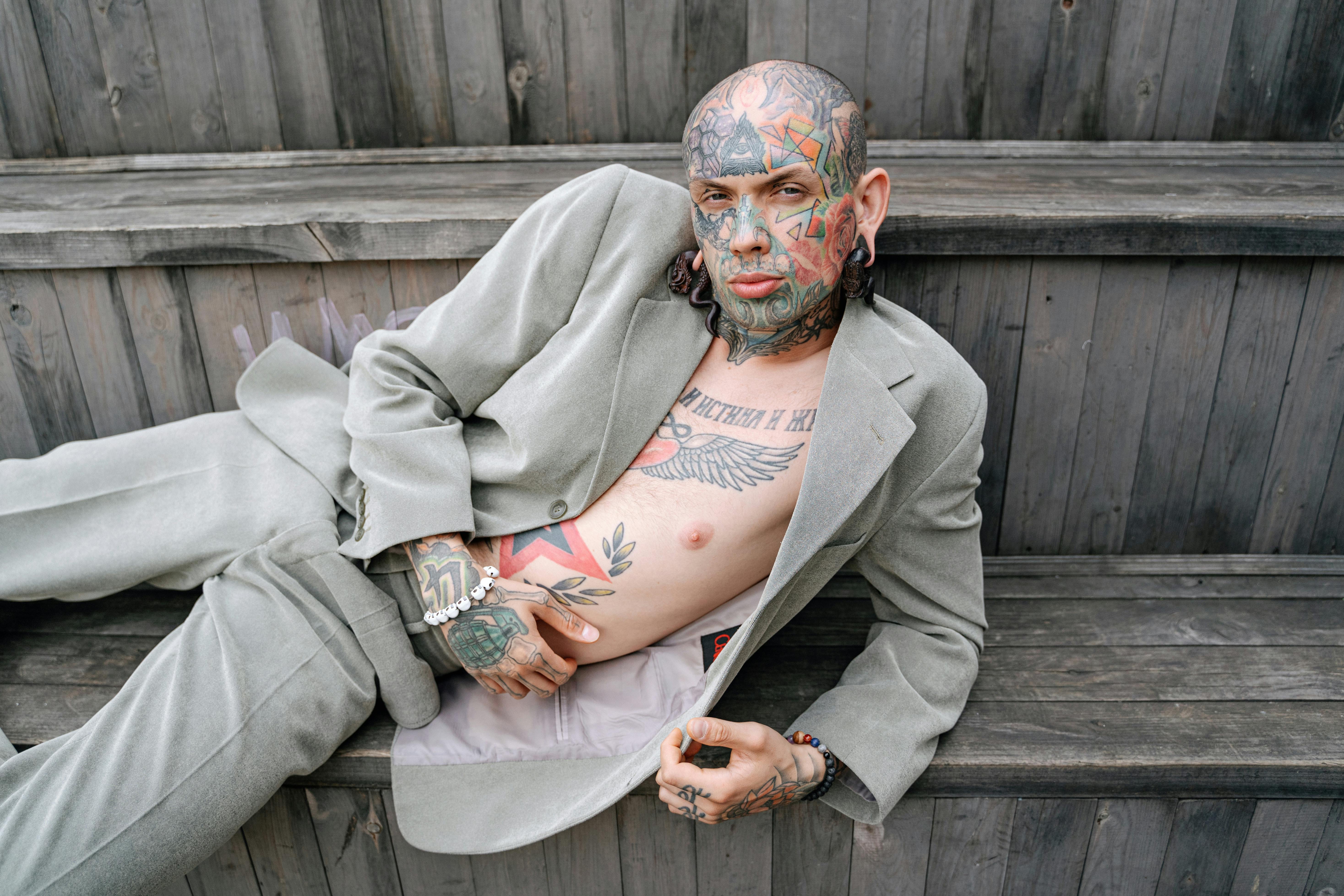Portrait of a tattooed man posing confidently on a wooden bench, showcasing body art.