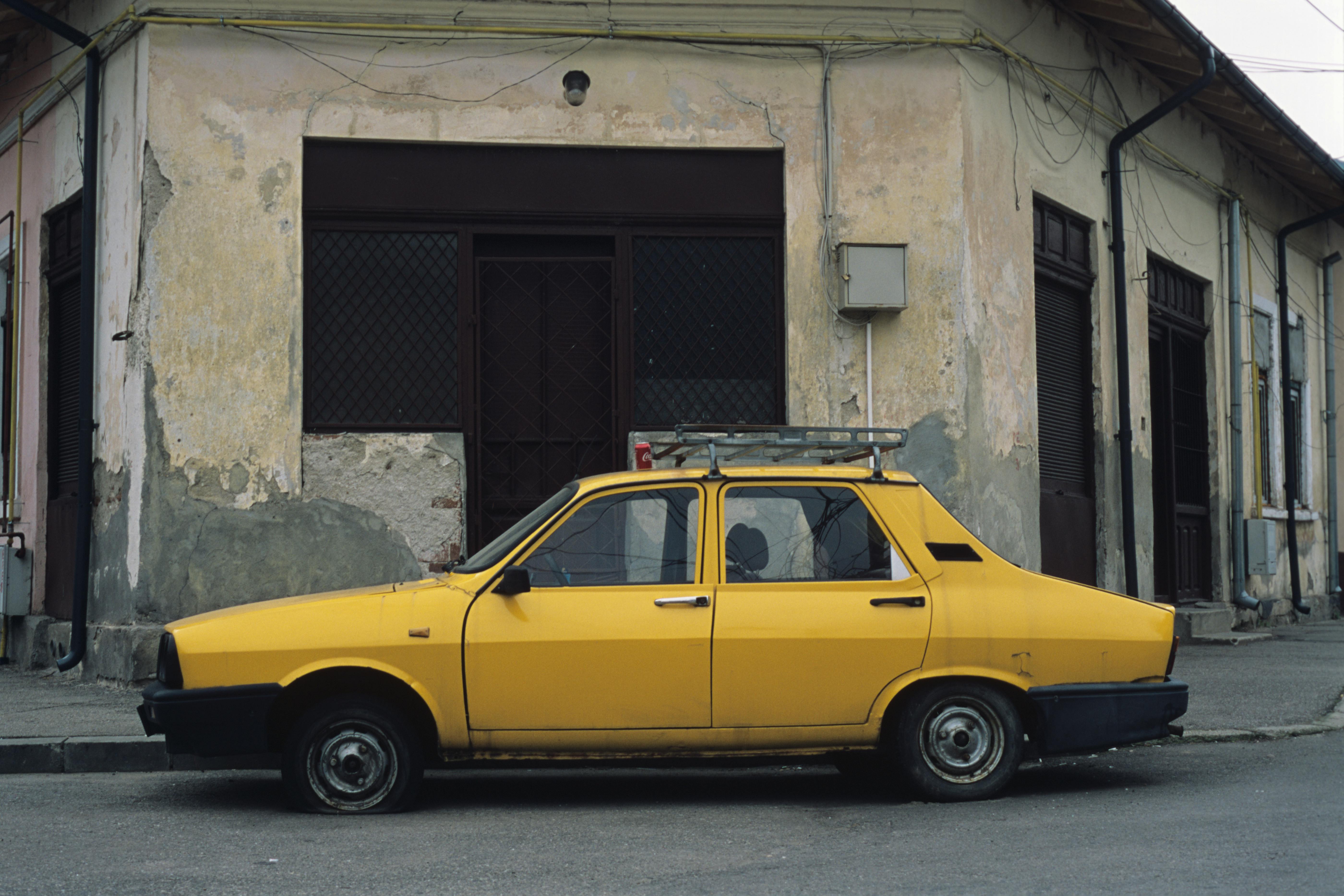 Yellow vintage car parked on a street in Bucharest, Romania, with a weathered building background.