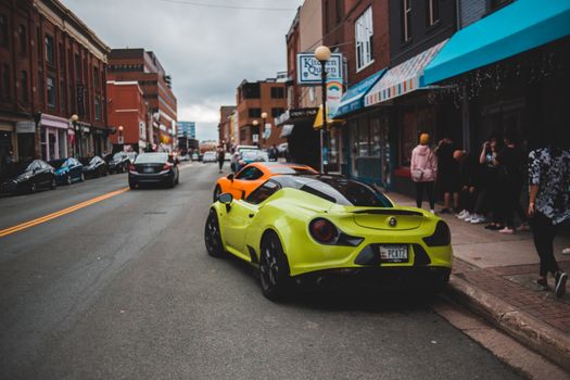 Colorful modern racing cars parked on asphalt road near sidewalk with unrecognizable people in town
