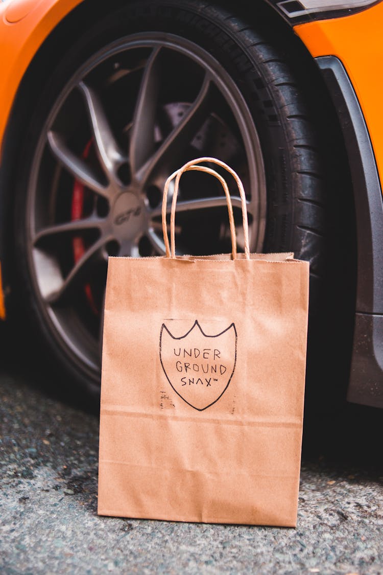 Paper Package Placed On Asphalt Near Wheel Of Modern Car