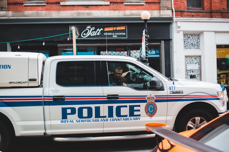 Policeman Sitting In Police Car Driving On Street