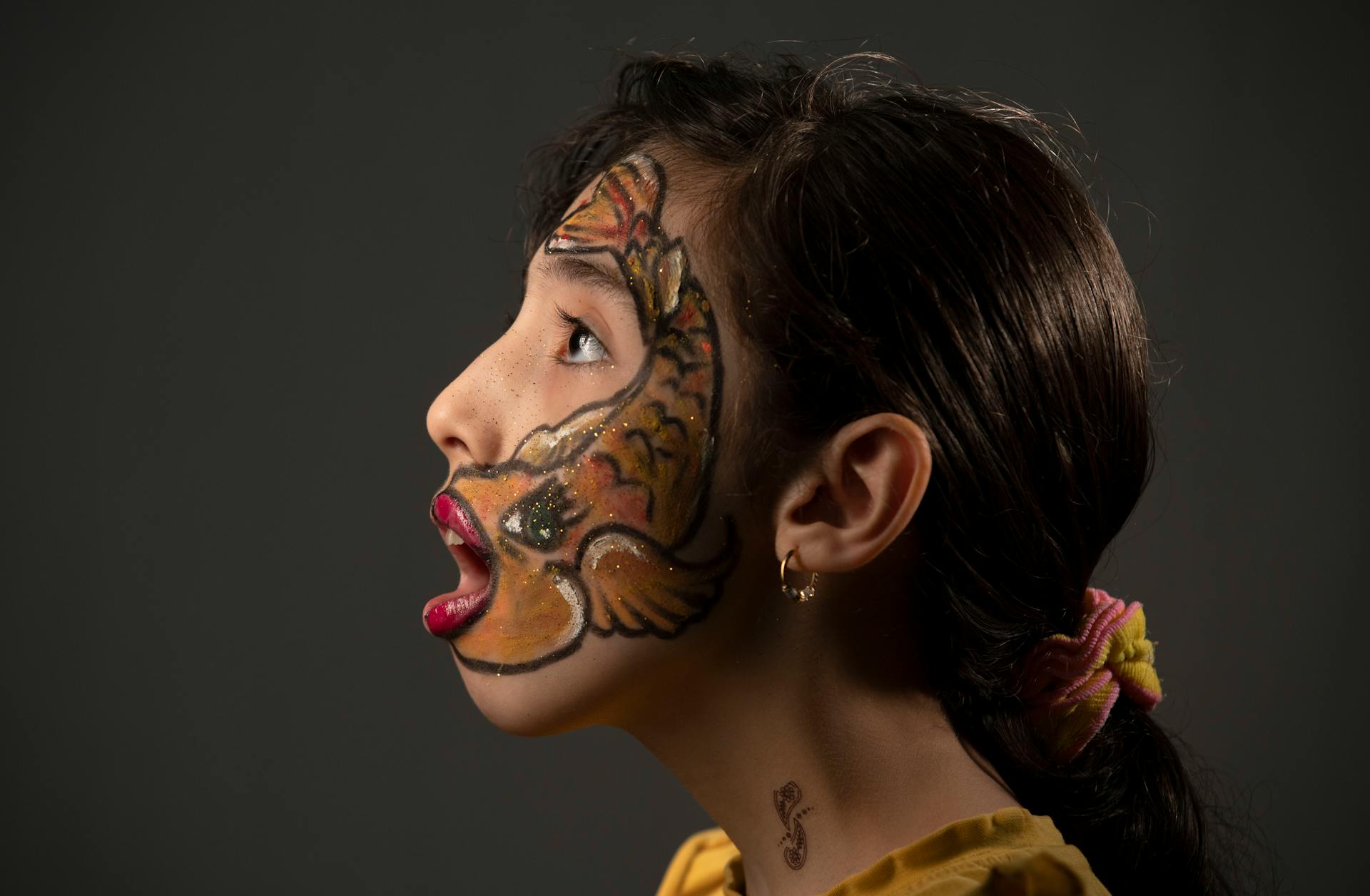 Side view portrait of a woman with colorful artistic fish face paint and accessories.