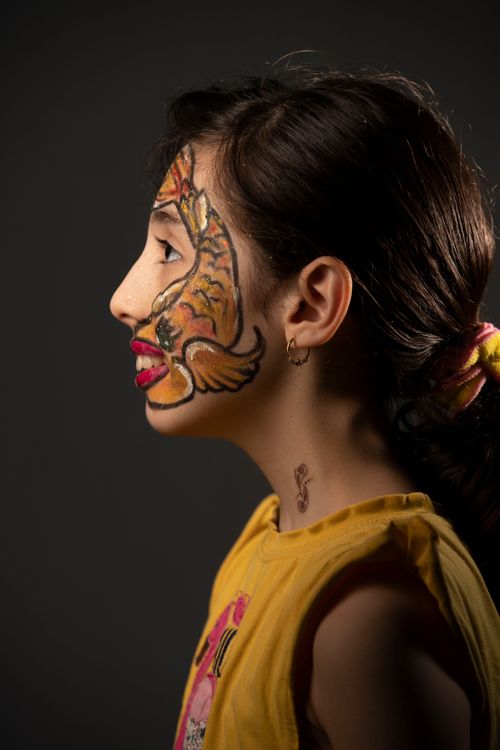 Free Side view portrait of a young girl with vibrant face painting against a gray background. Stock Photo