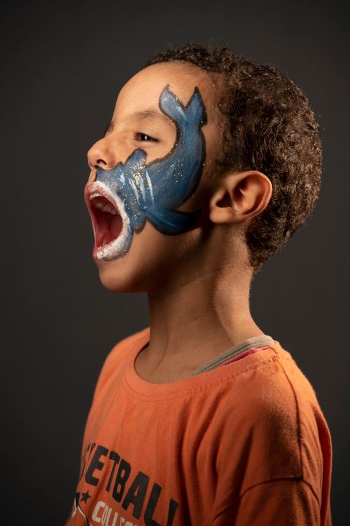 Free Side profile of a child in an orange shirt with artistic face paint and open mouth expressing joy. Stock Photo