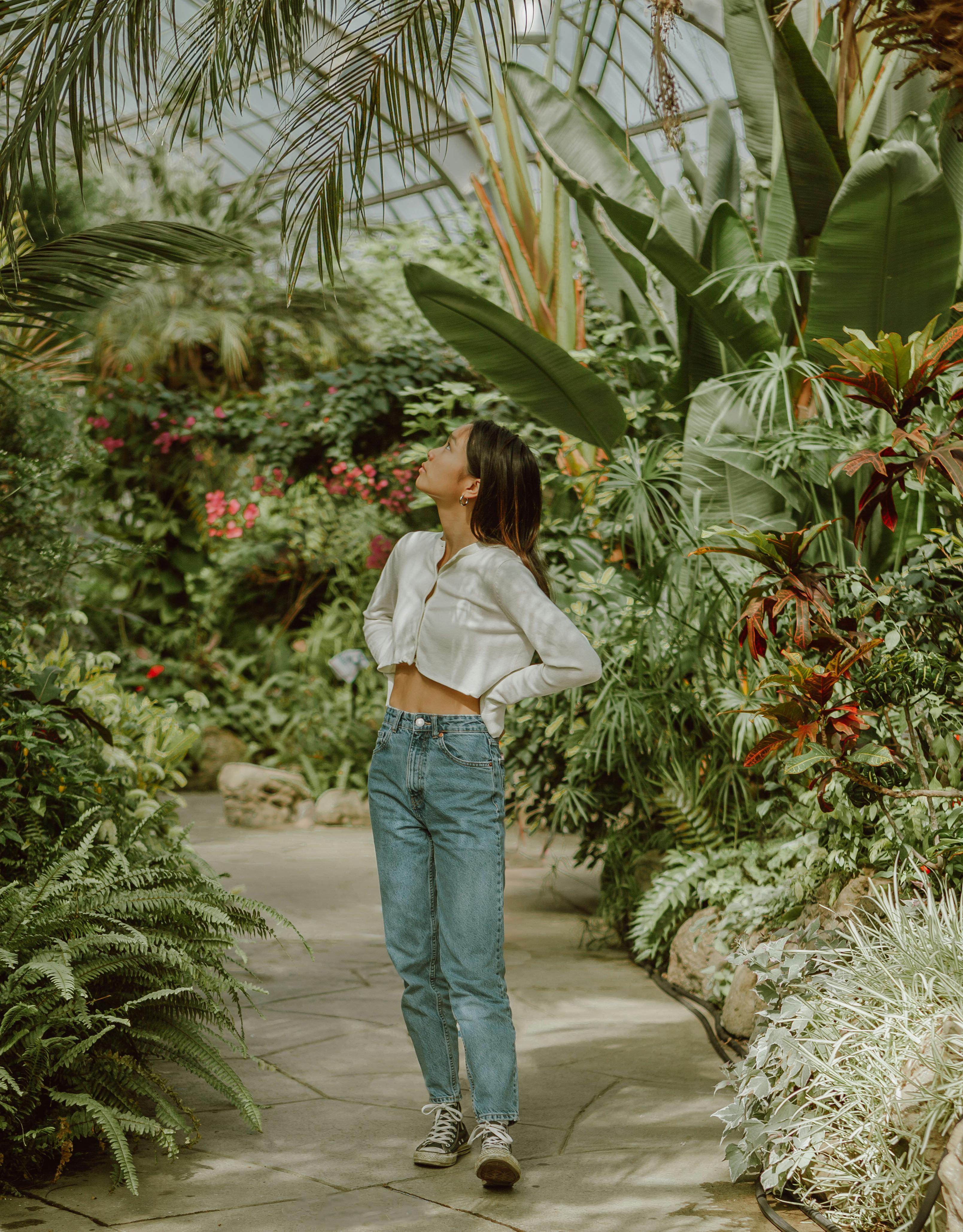 Attentive young Asian woman strolling along path in tropical greenhouse ...