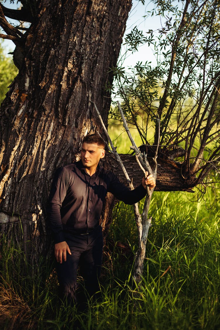 Young Man Standing At Big Tree In Fields