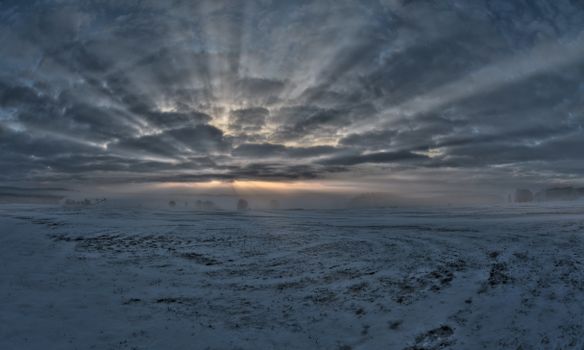Stunning winter sunrise with sun rays breaking through mist over snow-covered landscape.