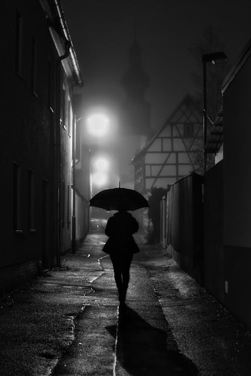 Monochrome Photo of a Person with an Umbrella Walking on an Alley