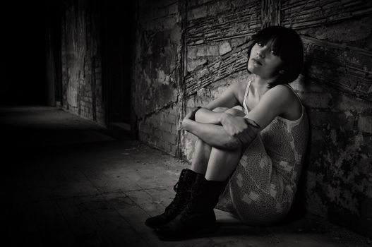 Black and white portrait of a woman sitting in an abandoned building. Moody and dramatic atmosphere.