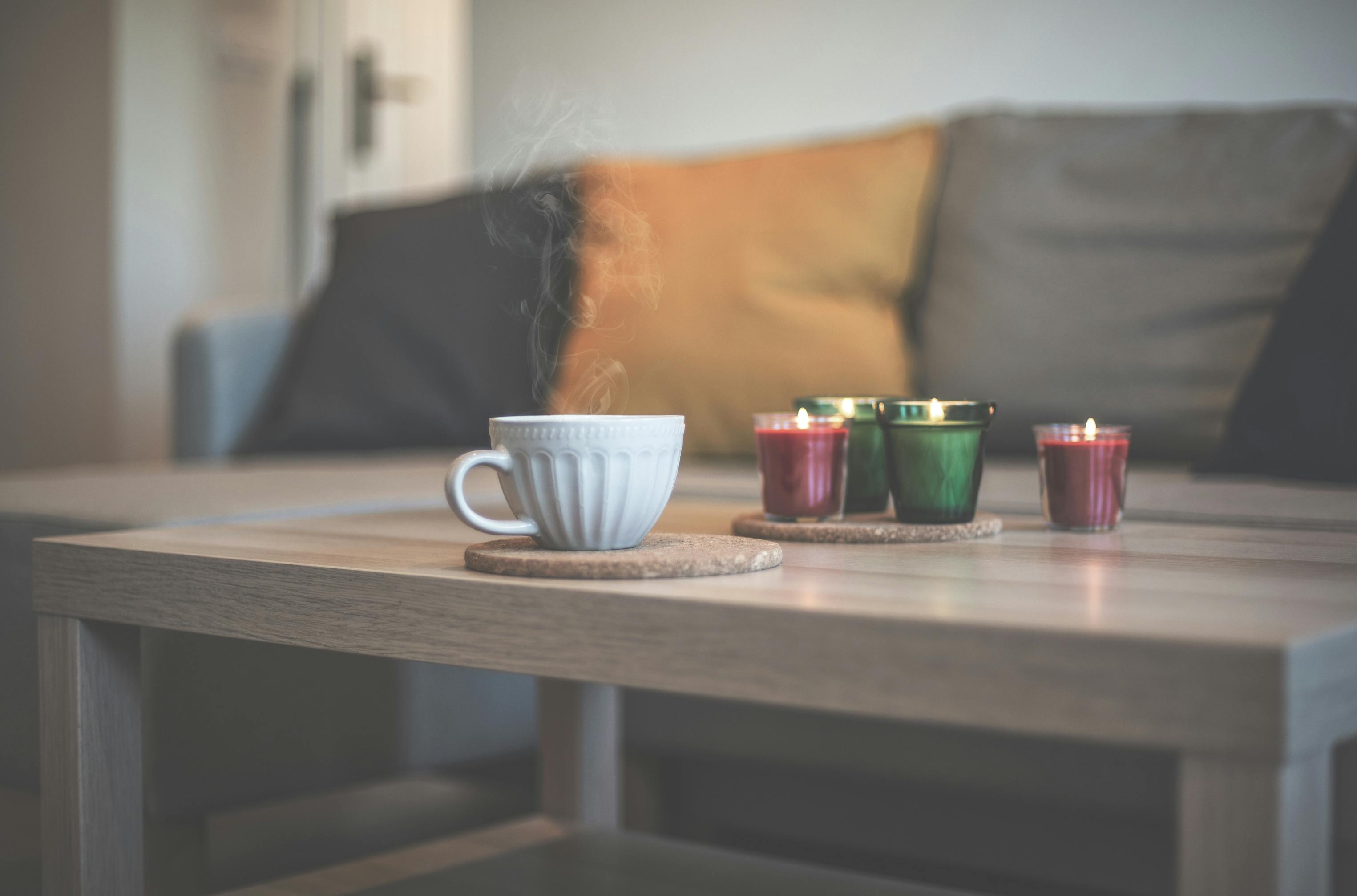 Warm and inviting living room scene featuring a steaming coffee cup and lit candles on a wooden table.