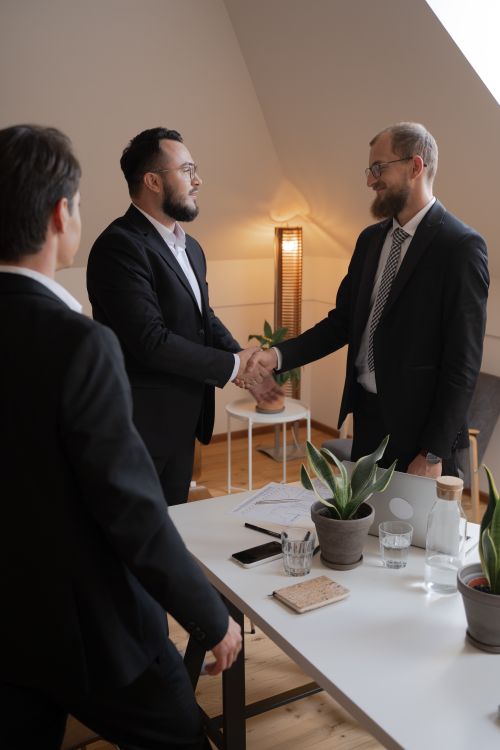Free Businessmen in formal attire shaking hands during a meeting in a modern office setting. Stock Photo